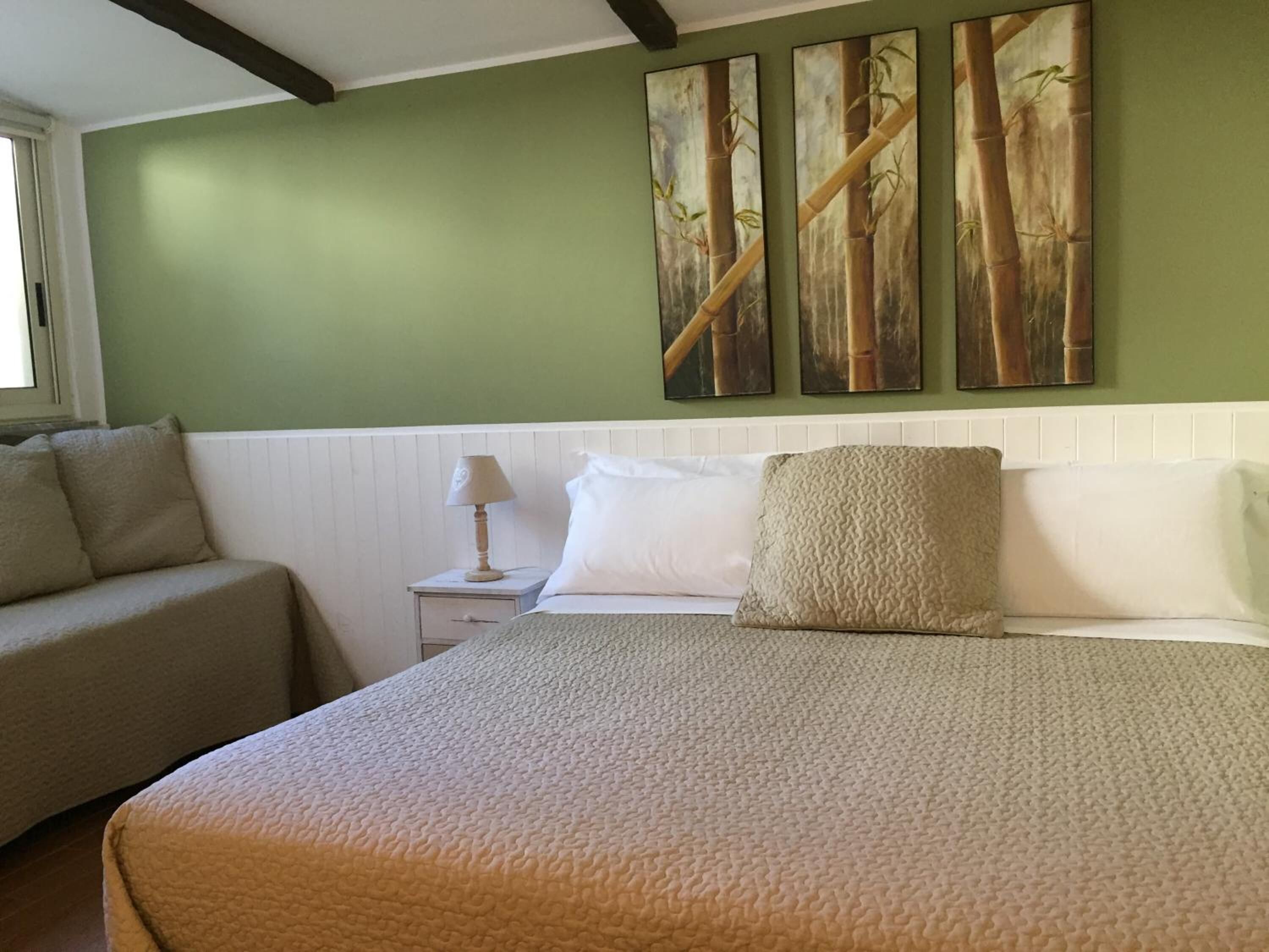 A bedroom with a bed, a nightstand, a lamp, a sofa, and three wall-mounted paintings.