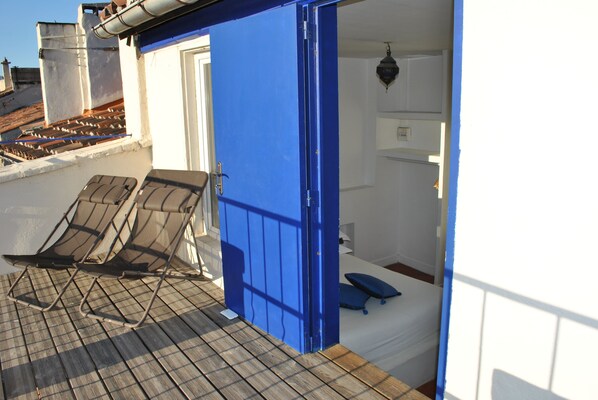 Una habitación con puerta azul, una cama con almohada azul y dos sillones en una terraza de madera.