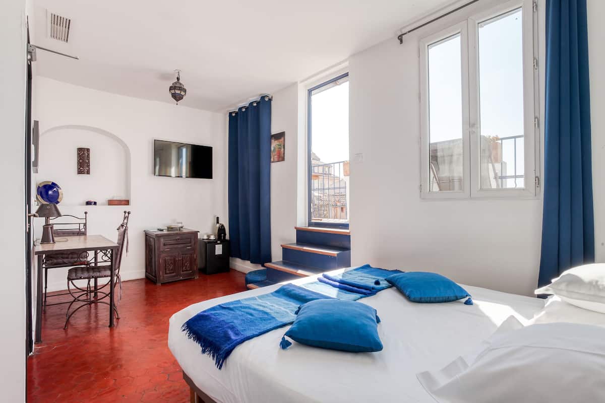 A bedroom with a bed, a desk, a chair, a TV, and a window with curtains.