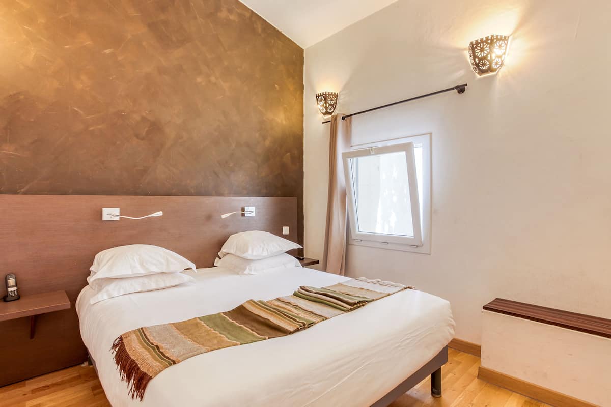 A neatly made bed with a striped blanket, a bedside table with a phone, and a wall-mounted light fixture.