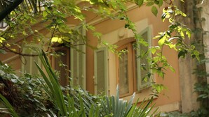 A building with a yellow facade and green shutters, surrounded by lush greenery. - Le Ryad Boutique Hôtel (Marseille)