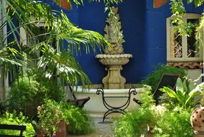 Un patio con una fuente, bancos y abundante vegetación.