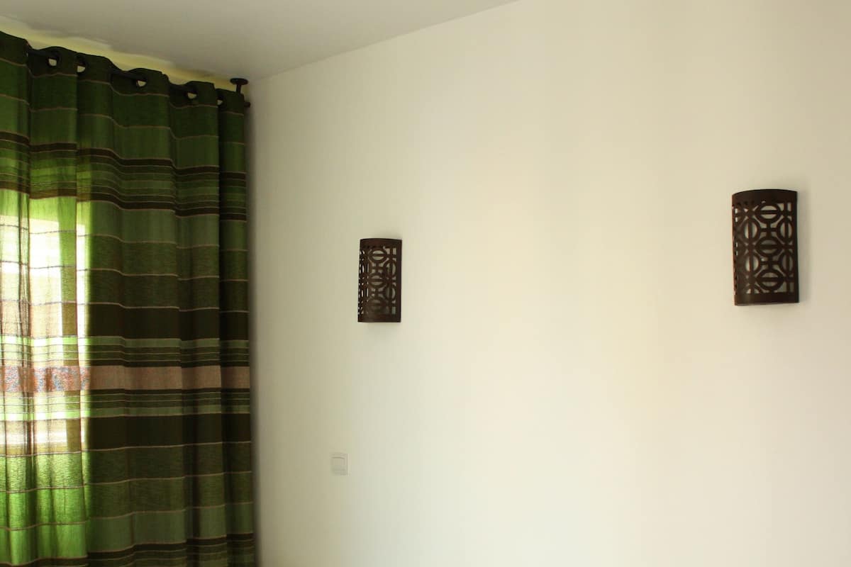 A bed with white linens, a green striped blanket, and a hanging light fixture above.