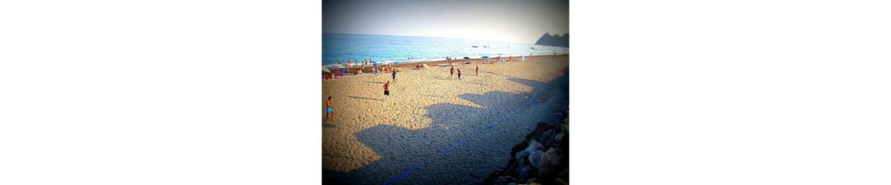 Una playa con gente jugando al voleibol y otros relajándose bajo sombrillas.
