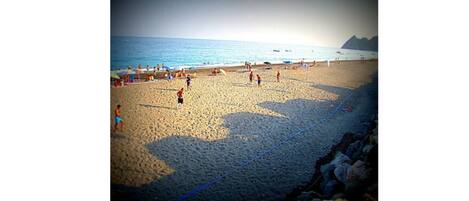 Una playa con gente jugando al voleibol y otros relajándose bajo sombrillas.