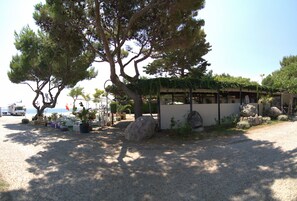 A building with a covered outdoor area, surrounded by large rocks and potted plants. - Camping La Focetta Sicula (Sant'Alessio Siculo)