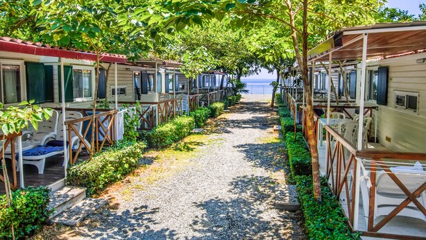 Een rij vakantiehuisjes in camperstijl met buiten zitplaatsen en een grindpad dat naar het strand leidt.