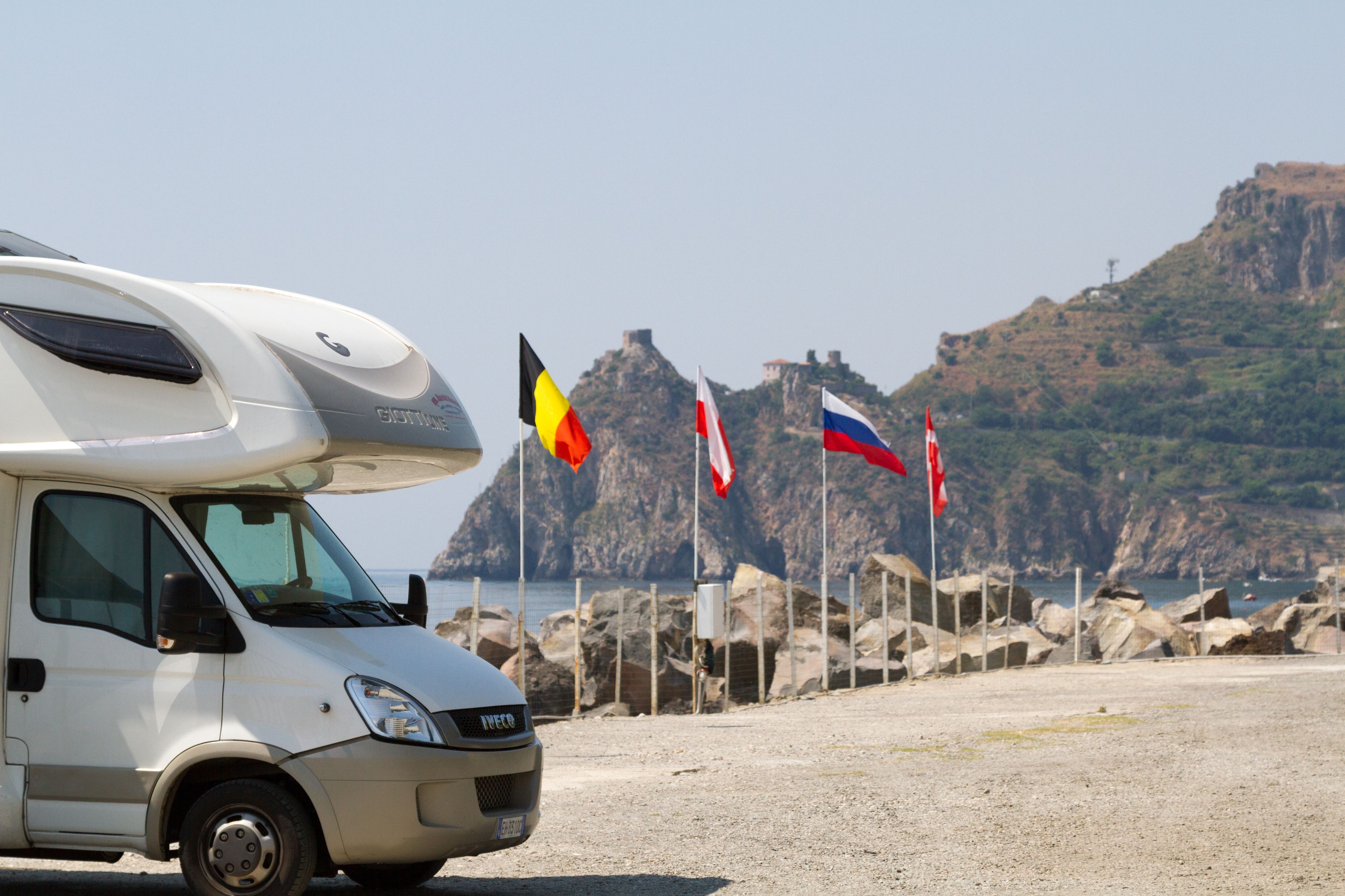 En hvid campingvogn parkeret på en grusstrand med flag i baggrunden.