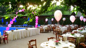 An outdoor dining area with round tables and chairs, decorated with pink balloons and blue umbrellas.