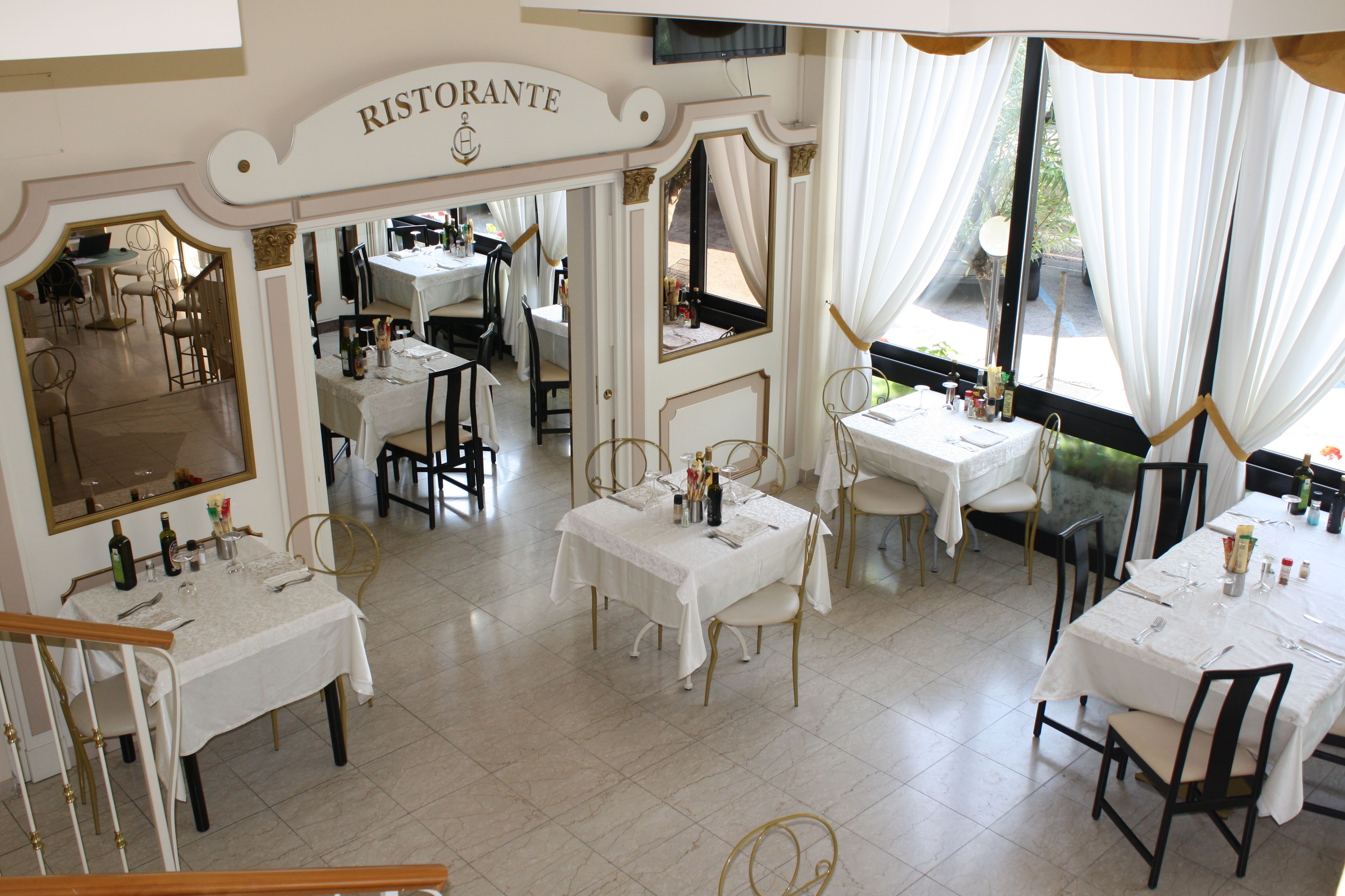 Interno di un ristorante con diversi tavoli, sedie e un cartello con la scritta 'RISTORANTE'.