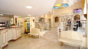 A spacious hotel lobby with a marble floor, a central staircase, and a seating area with white benches. - Hotel Ristorante Commercio (Salò)