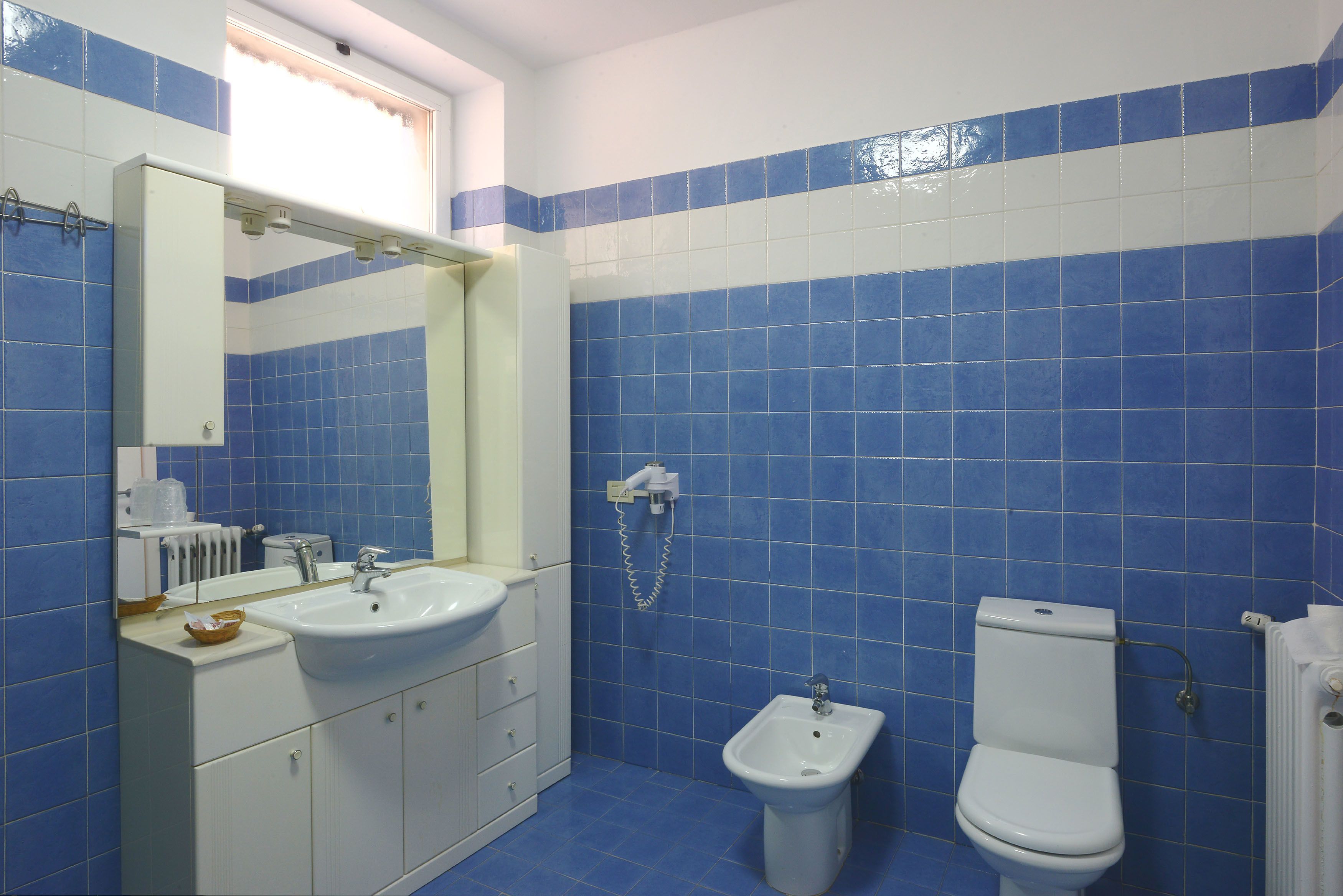 A bathroom with blue tiles, a white sink, a bidet, and a toilet.