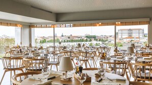 A restaurant with multiple tables and chairs, large windows offering a city view. - Villa C Boutique Hotel (Vila do Conde)