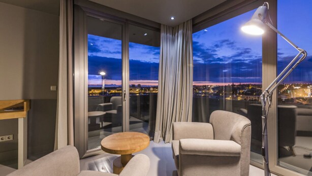 A modern hotel room with a balcony, large windows, and a view of the cityscape at dusk. - Villa C Boutique Hotel (Vila do Conde)