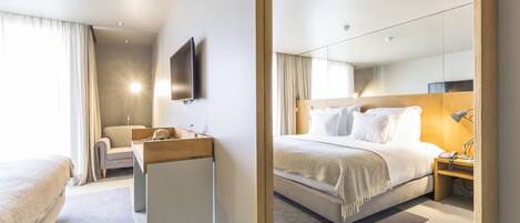 Une chambre d’hôtel moderne avec un grand lit, une table de chevet avec une lampe, une commode en bois, un téléviseur intégré et un grand miroir.