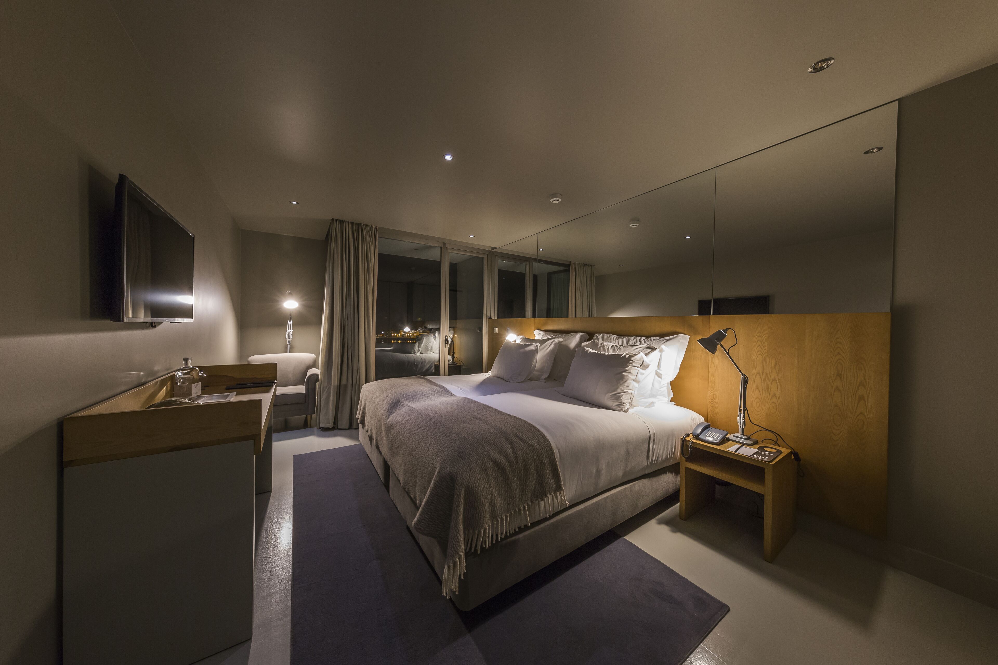A modern hotel room with a large bed, bedside table, and a TV mounted on the wall.