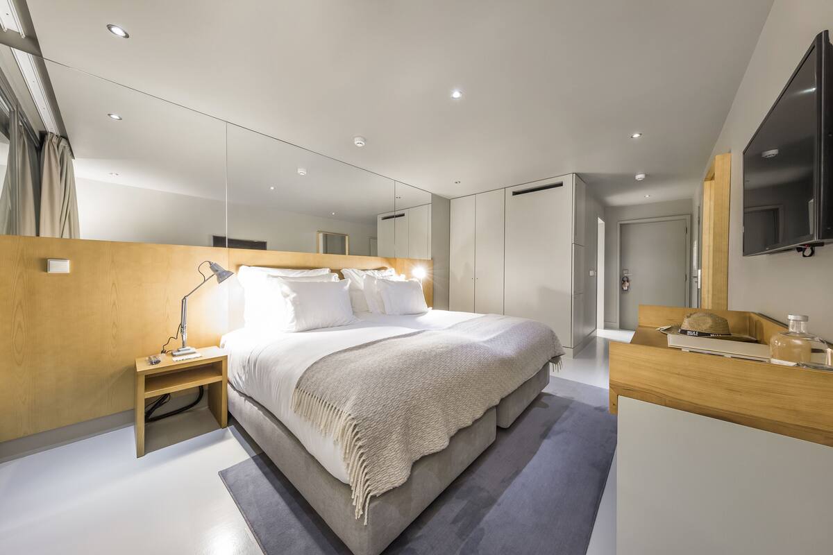 A modern bedroom with a large bed, bedside tables, a desk, and a TV.