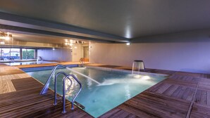 An indoor swimming pool with wooden decking, a water fountain, and a view of the outside. - Villa C Boutique Hotel (Vila do Conde)