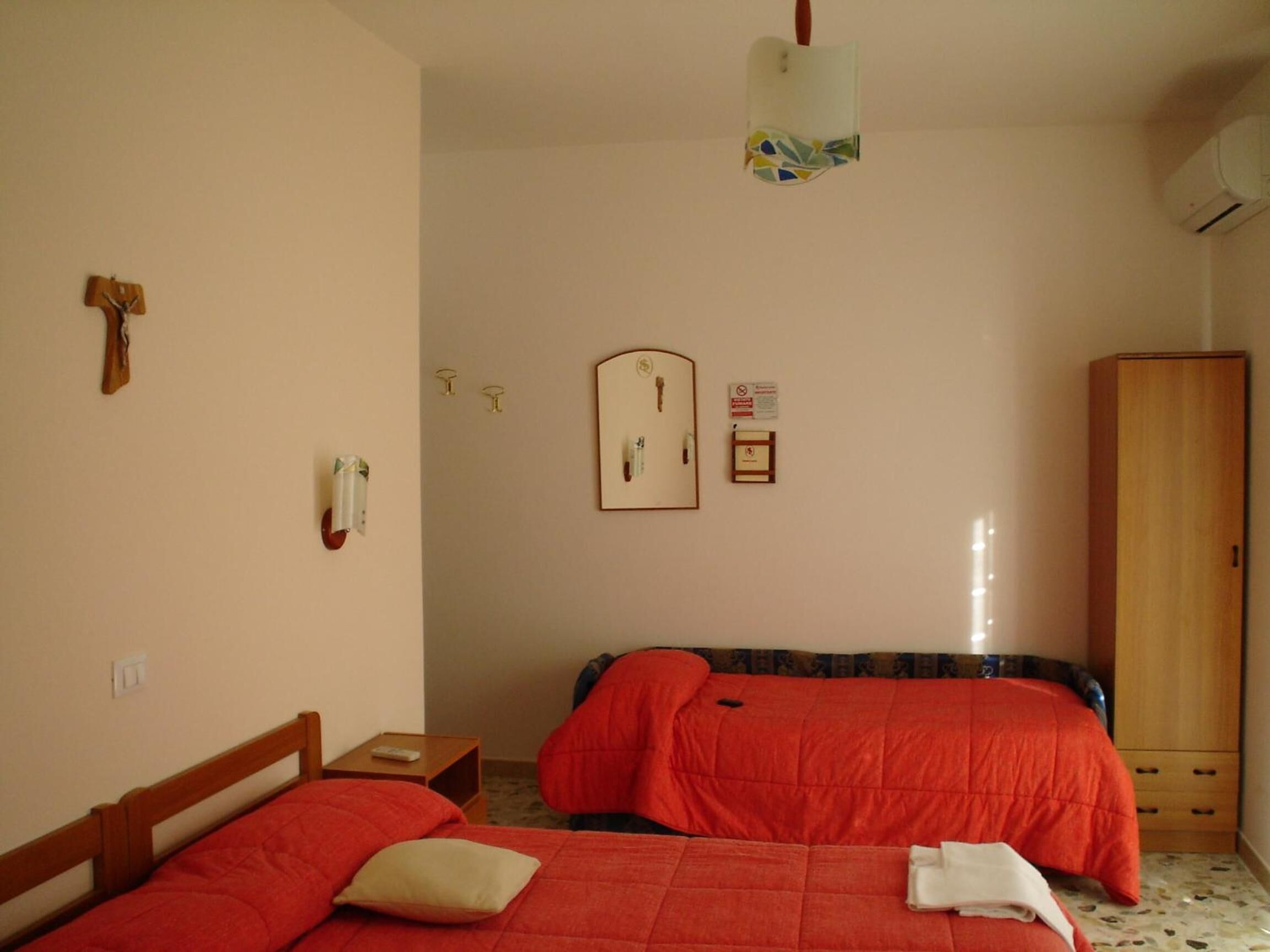 Een slaapkamer met twee bedden, een houten garderobe, een spiegel aan de muur en een klein nachtkastje.