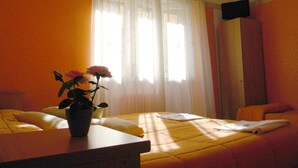 Une chambre d’hôtel avec un lit, une table de chevet ornée d’un vase de fleurs, une chaise et un téléviseur fixé au mur.
