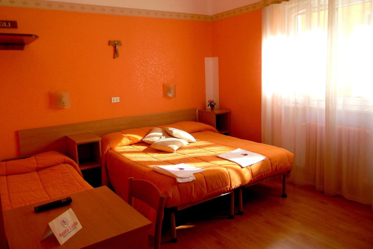 A hotel room with an orange theme, including an orange bed, matching headboard, and a small table with a sign.
