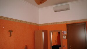 Une pièce aux murs orange, avec une porte en bois, un petit bureau avec une chaise et un téléviseur fixé au mur.