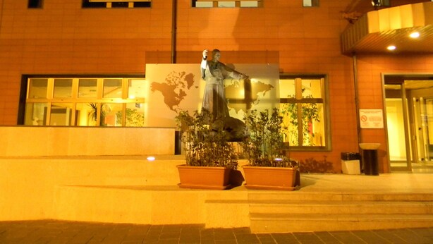 Une statue se trouve devant un bâtiment doté de grandes fenêtres et orné d’une fresque représentant une carte.