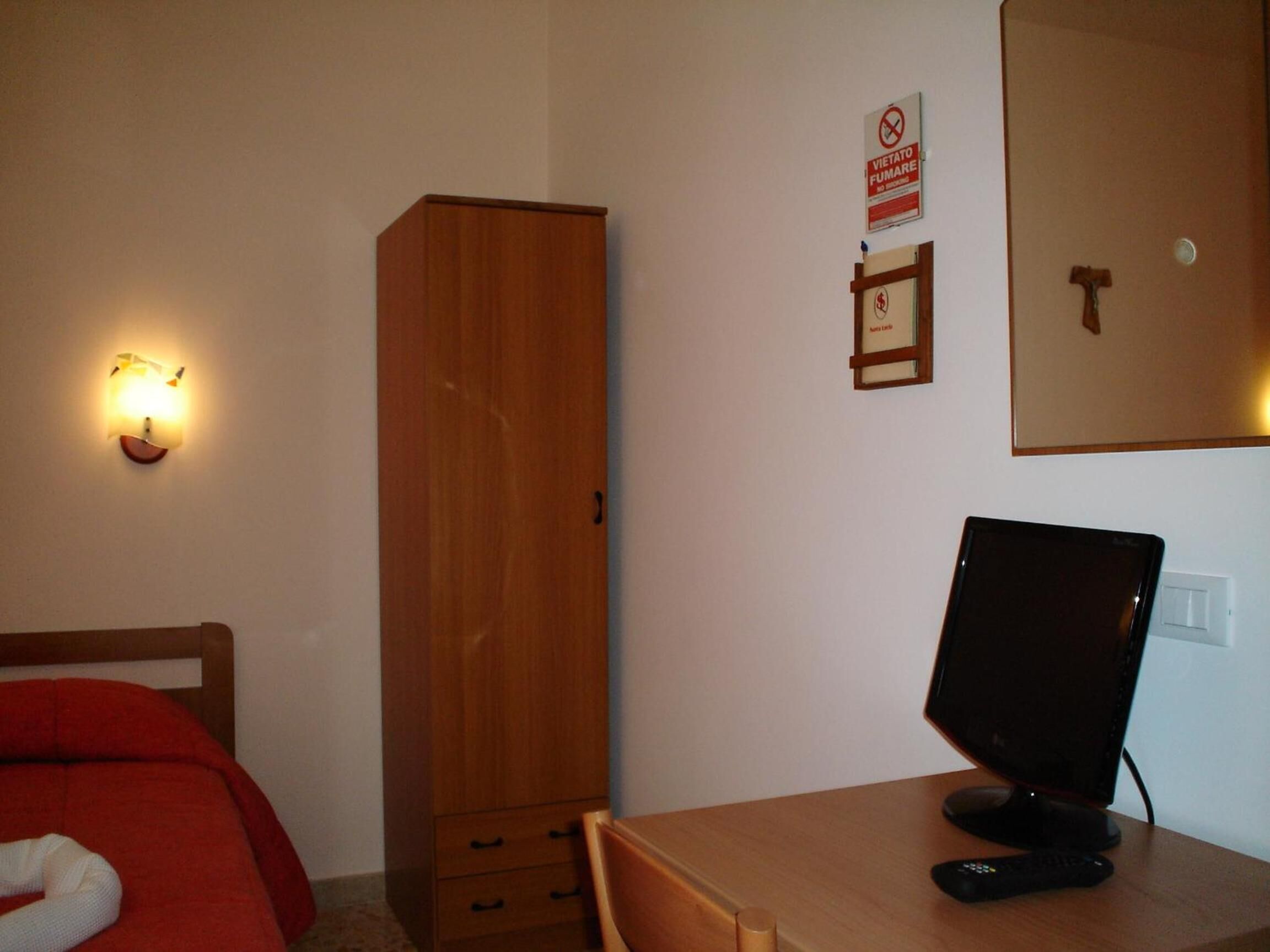 Un dormitorio con un armario de madera, un escritorio con computadora, una silla y una cama con manta roja.