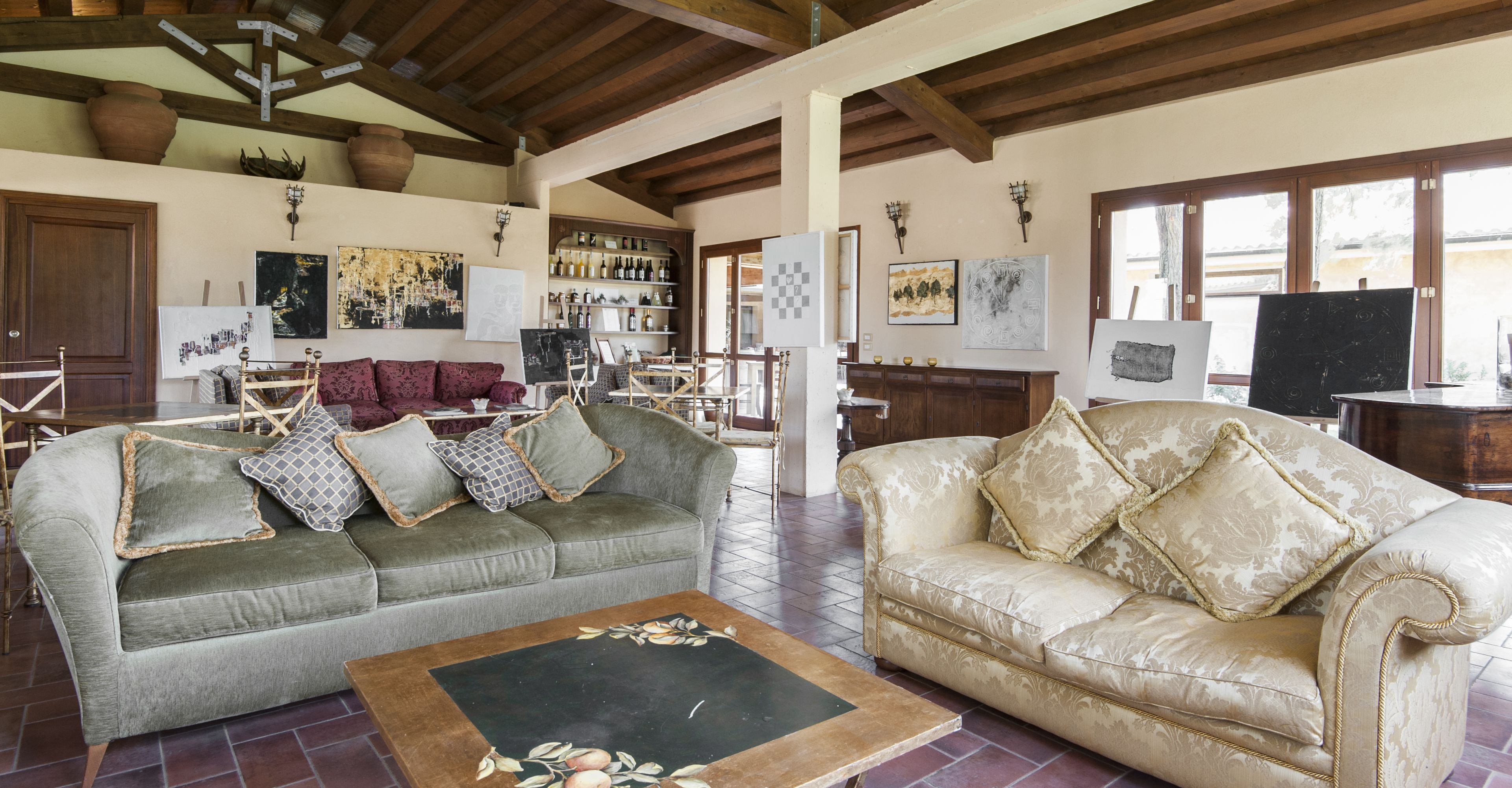 Un salón amplio con dos sofás, una mesa de centro y una chimenea. Varias pinturas decoran las paredes y se aprecia una estantería para vinos al fondo.