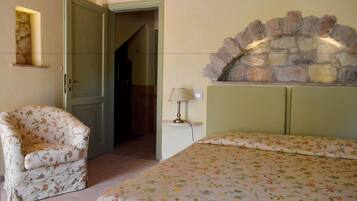 A bedroom with a floral bedspread, a chair, a stone fireplace, and a lamp.