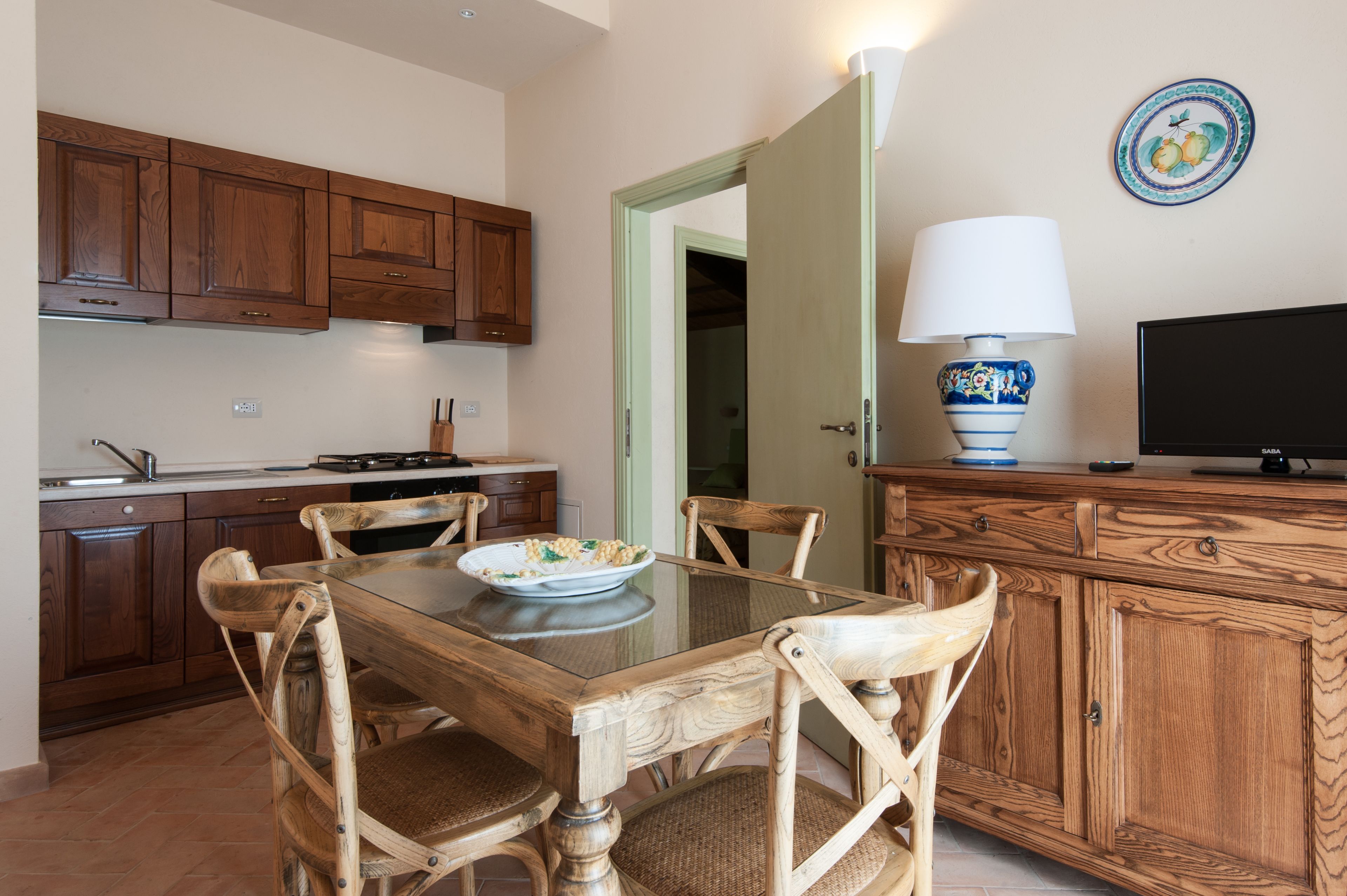 A kitchen with wooden cabinets, a dining table with chairs, a television, and a lamp.