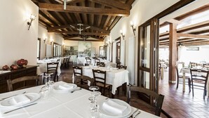 A dining area with tables set for service, wooden beams on the ceiling, and a view of the outdoors. - Tenuta Uccellina (Magliano in Toscana)