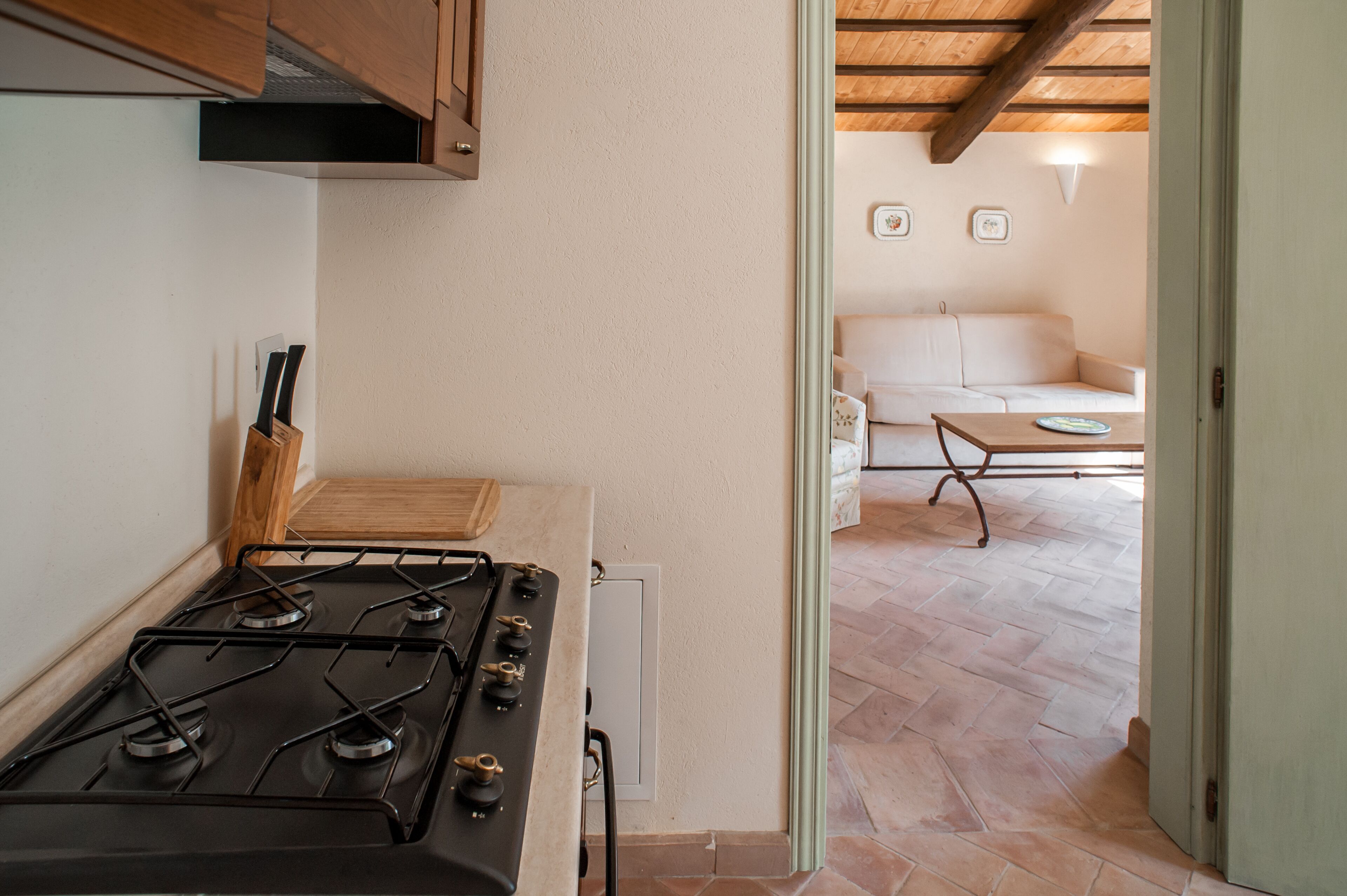 Eine Küche mit Herd, Holzschränken und Blick in einen Wohnbereich mit Sofa und Tisch.