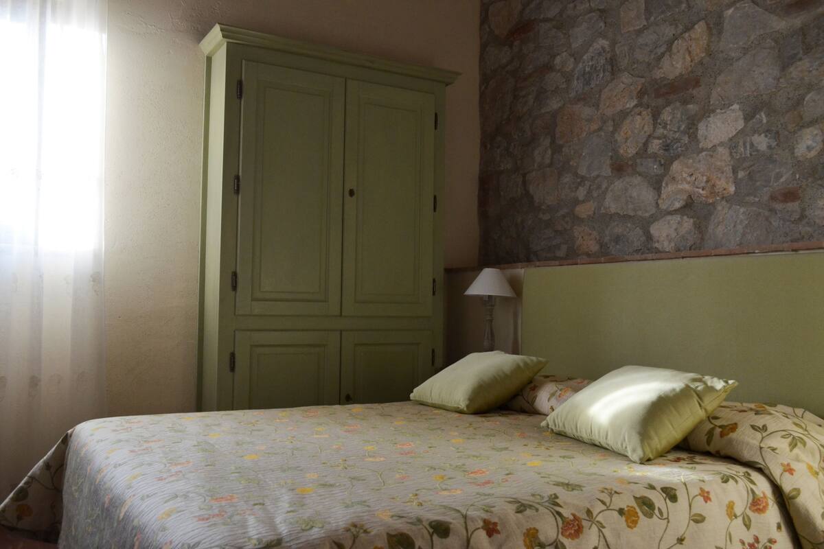 A bedroom with a bed, a green wardrobe, and a stone wall.