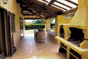 A covered patio with a brick floor, a wooden barrel, a table with chairs, and a brick oven. - Tenuta Uccellina (Magliano in Toscana)
