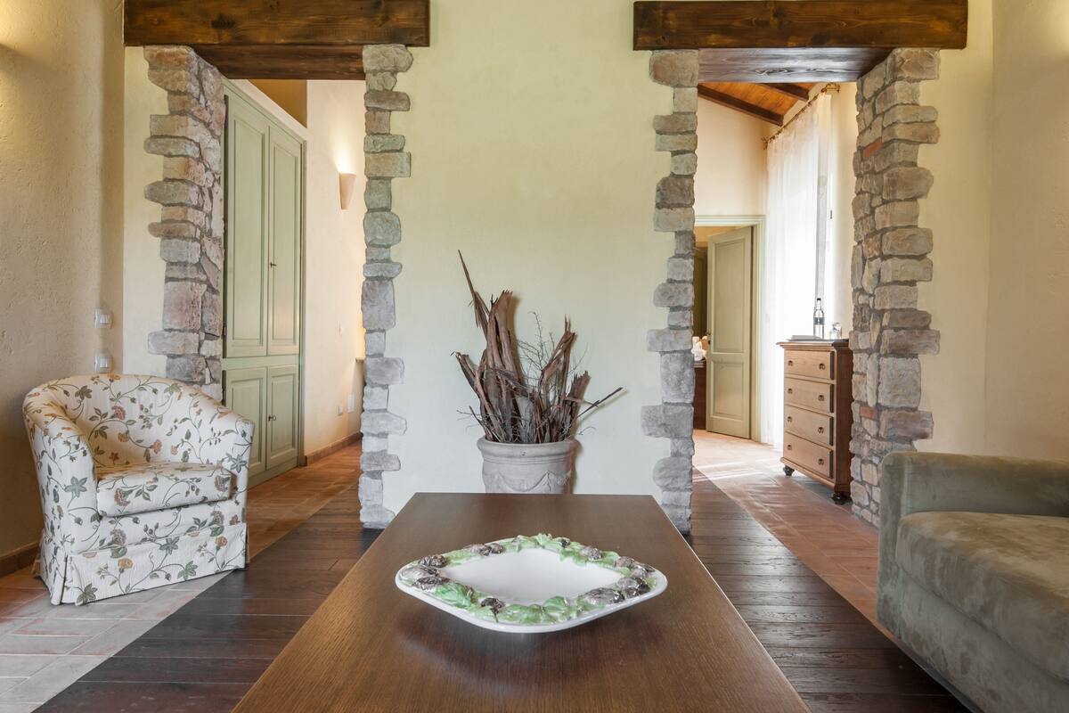 A room with a wooden table, stone pillars, a floral armchair, and a sofa.