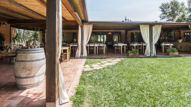 An outdoor patio with tables and chairs, a wooden barrel, and a grassy area. - Tenuta Uccellina (Magliano in Toscana)