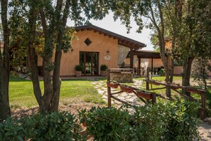 A rustic building with a stone foundation, surrounded by a garden with potted plants and a wooden fence. - Tenuta Uccellina (Magliano in Toscana)