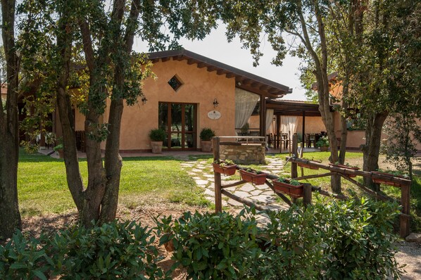 A rustic building with a stone foundation, surrounded by a garden with potted plants and a wooden fence.