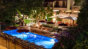 A nighttime swimming pool area with lounge chairs and umbrellas, surrounded by trees and plants. - Hotel Principe (Sanremo)