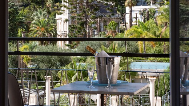 A terrace with tables and chairs, overlooking a cityscape with buildings and trees. - Hotel Principe (Sanremo)