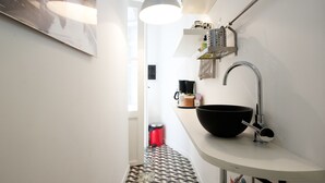 A narrow kitchen with a large black bowl on the counter, a hanging light fixture, and a red trash bin. - Colosseum Garden (Rome)