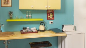 A kitchen with teal walls, yellow cabinets, a yellow countertop, a kettle, a toaster, and a coffee sign. - Colosseum Garden (Rome)