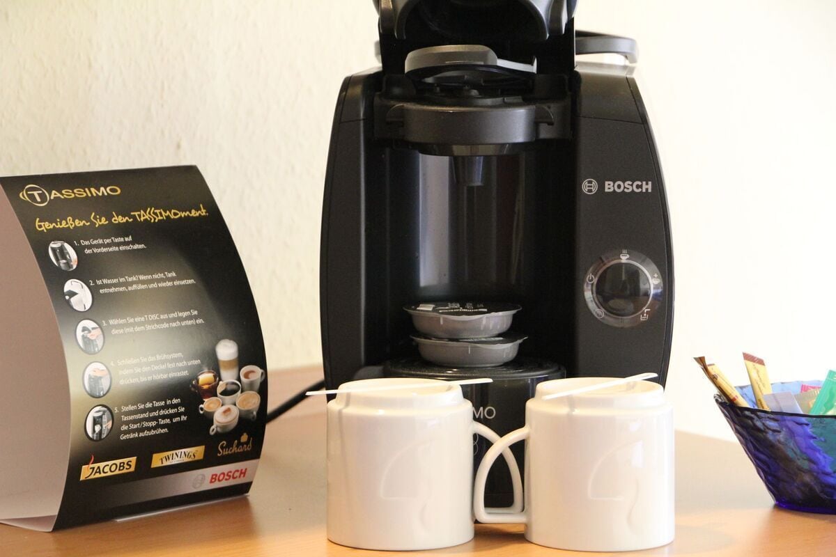 Una cafetera, un manual, dos tazas blancas y un portalápices azul con bolígrafos.