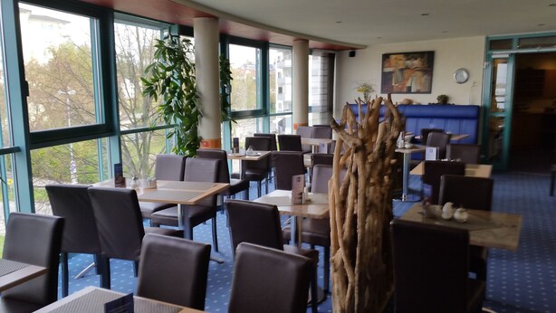 Un restaurante con mesas dentro, ventanas amplias y vistas al exterior.