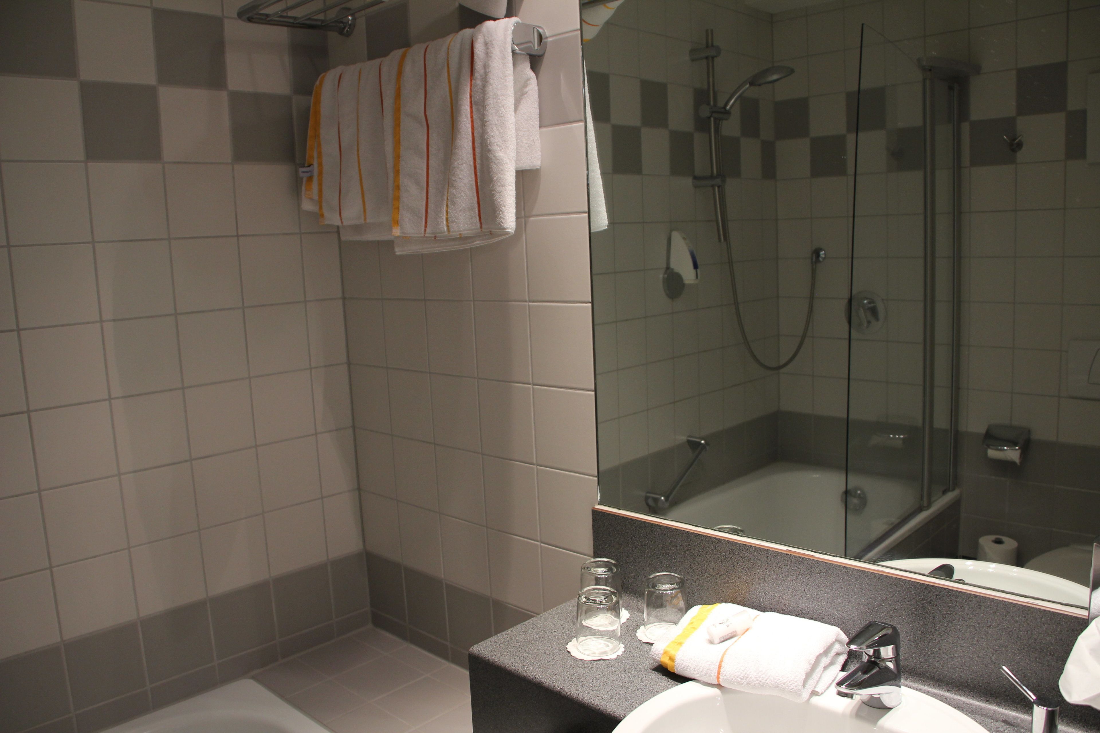 A modern bathroom with a glass-enclosed shower, a large mirror, and a countertop with a sink and toiletries.