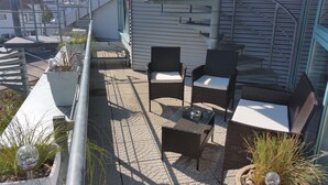 Una terraza en la azotea con mobiliario de mimbre, plantas en macetas y barandilla de metal.