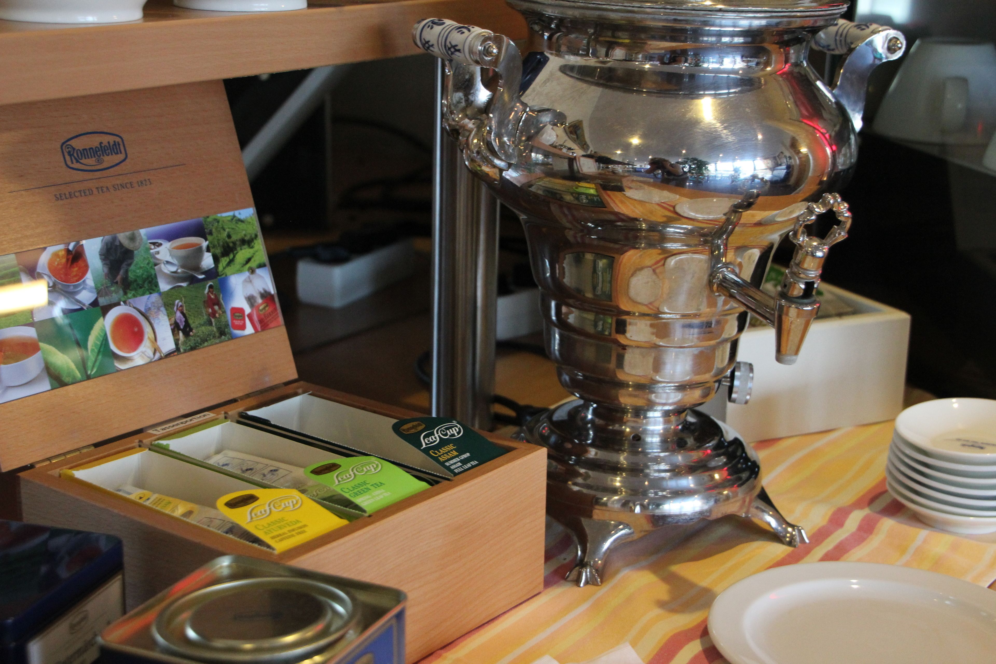 A silver samovar with tea bags and a tray of white plates on a table.