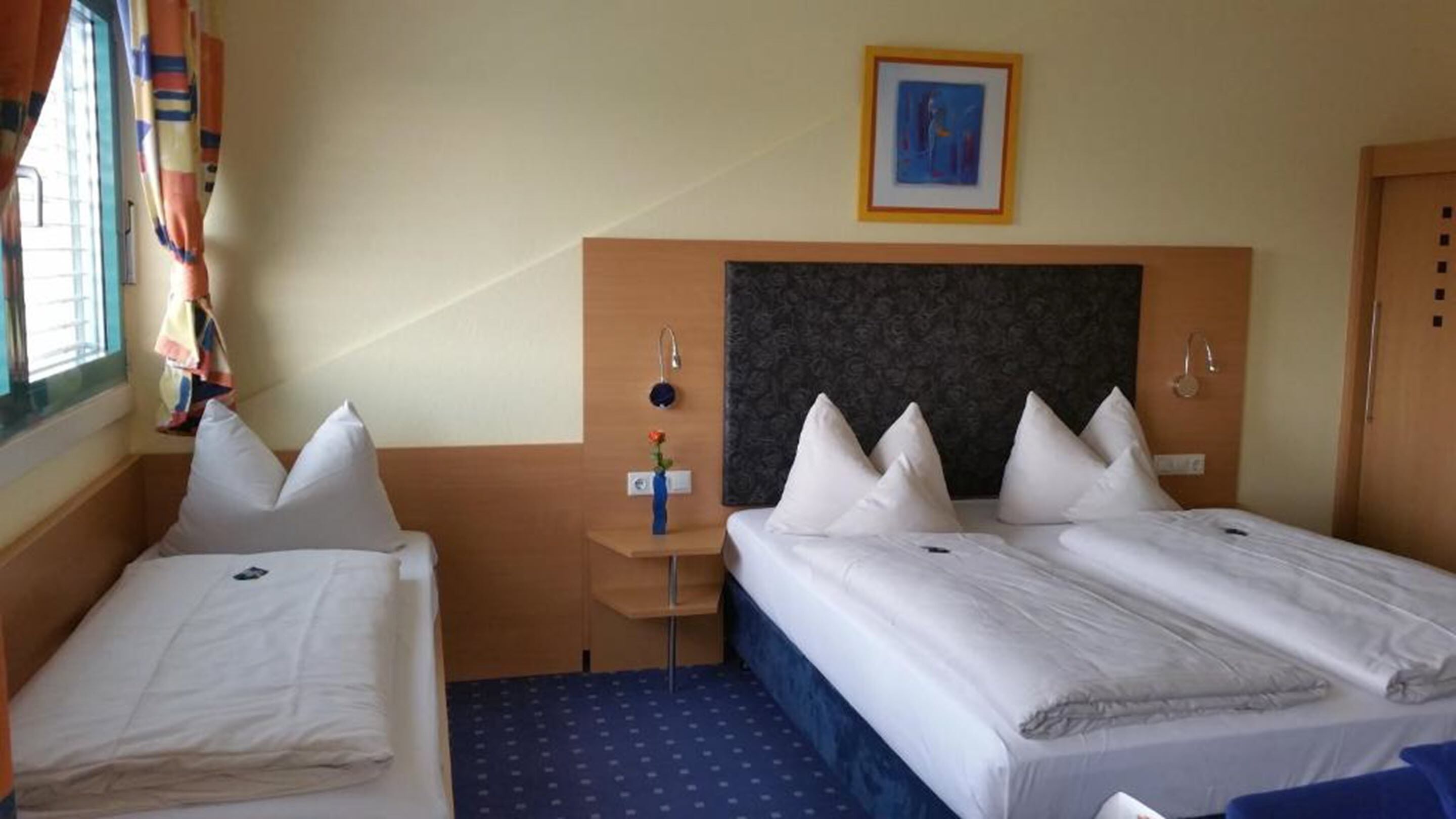 Habitación de hotel con dos camas, una mesita de noche, un cuadro y una ventana con cortinas.