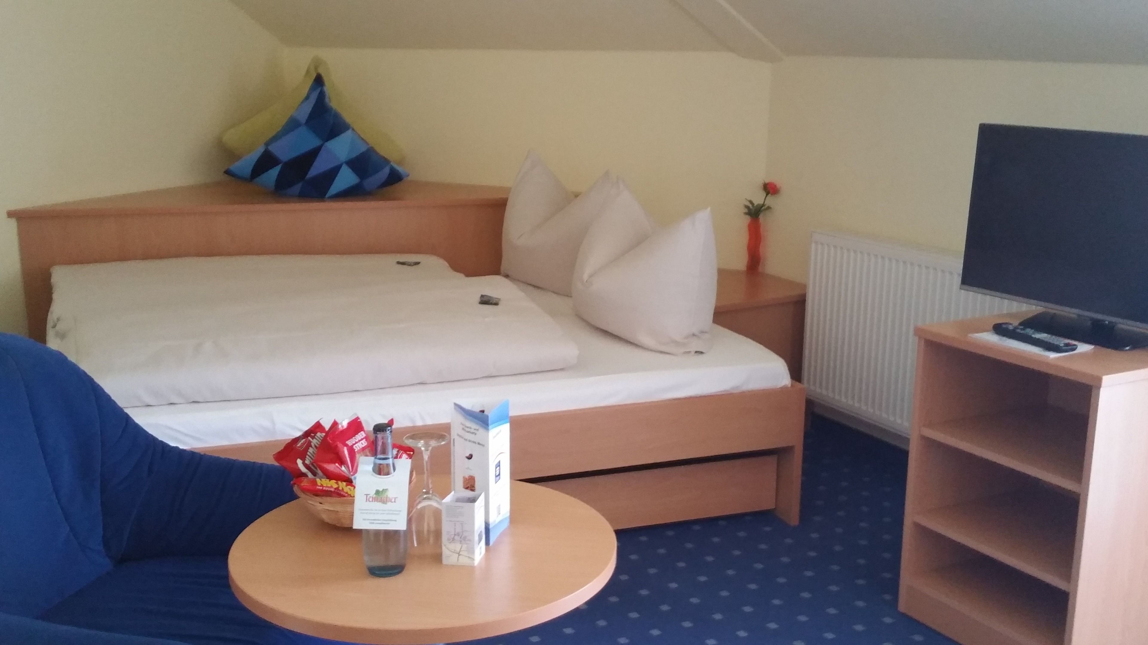 A hotel room with a bed, a TV, a small table with snacks, and a blue chair.